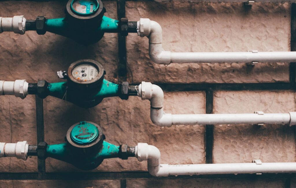 A vertical shot of residential water meters and pipes on stone wall background